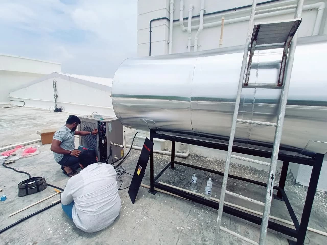 Heat pump equipment being installed beside an insulated hot-water storage tank